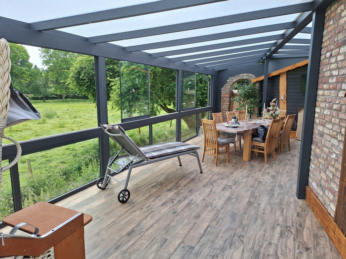 Kaltwintergarten mit verglasten Seitenwänden aus Aluminium in Anthrazit, Esstisch und Liege mit Blick in den Garten